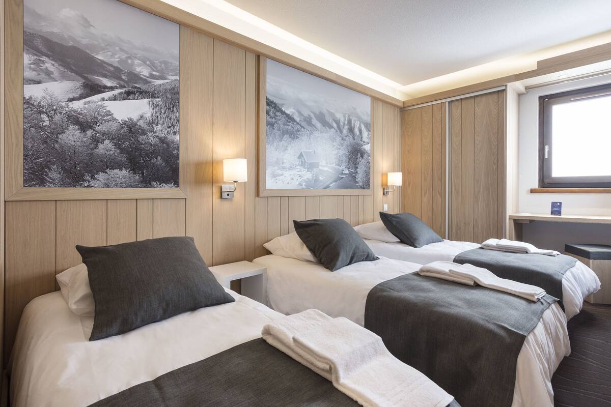 Habitación de hotel con dos camas, paneles de madera y grandes pinturas de paisajes en las paredes.