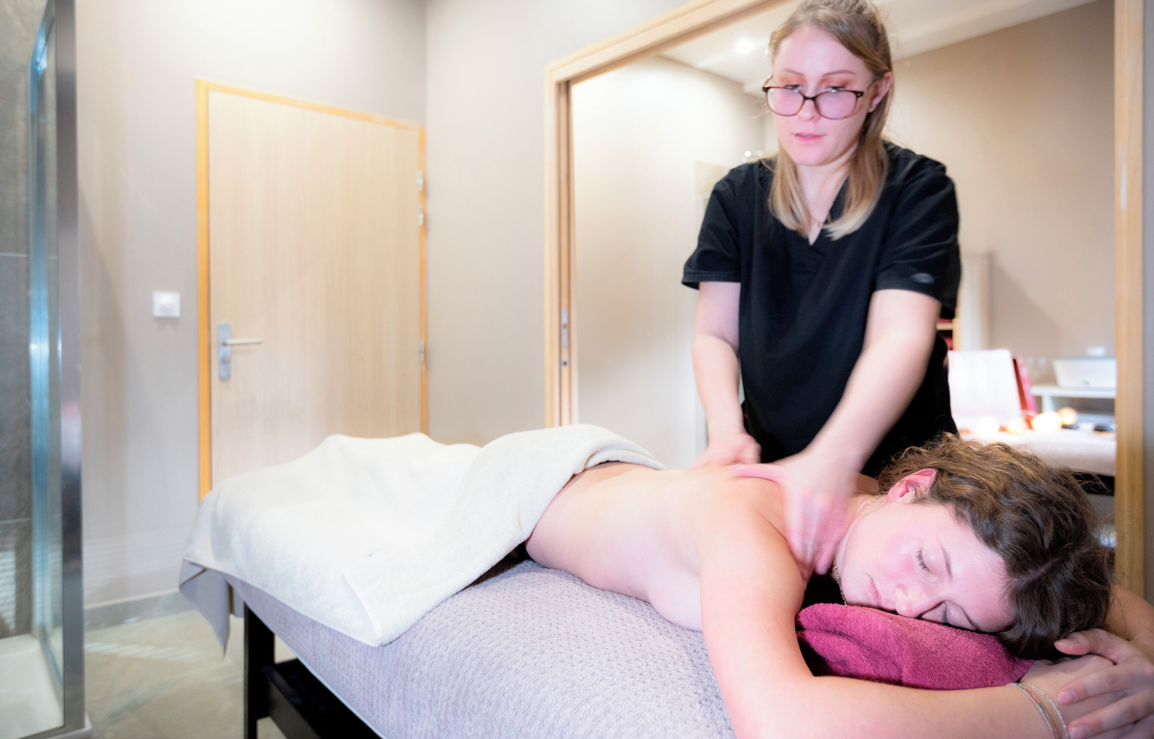 Une salle de massage équipée d’une table de massage, avec un client allongé sur le ventre et un thérapeute debout à côté.