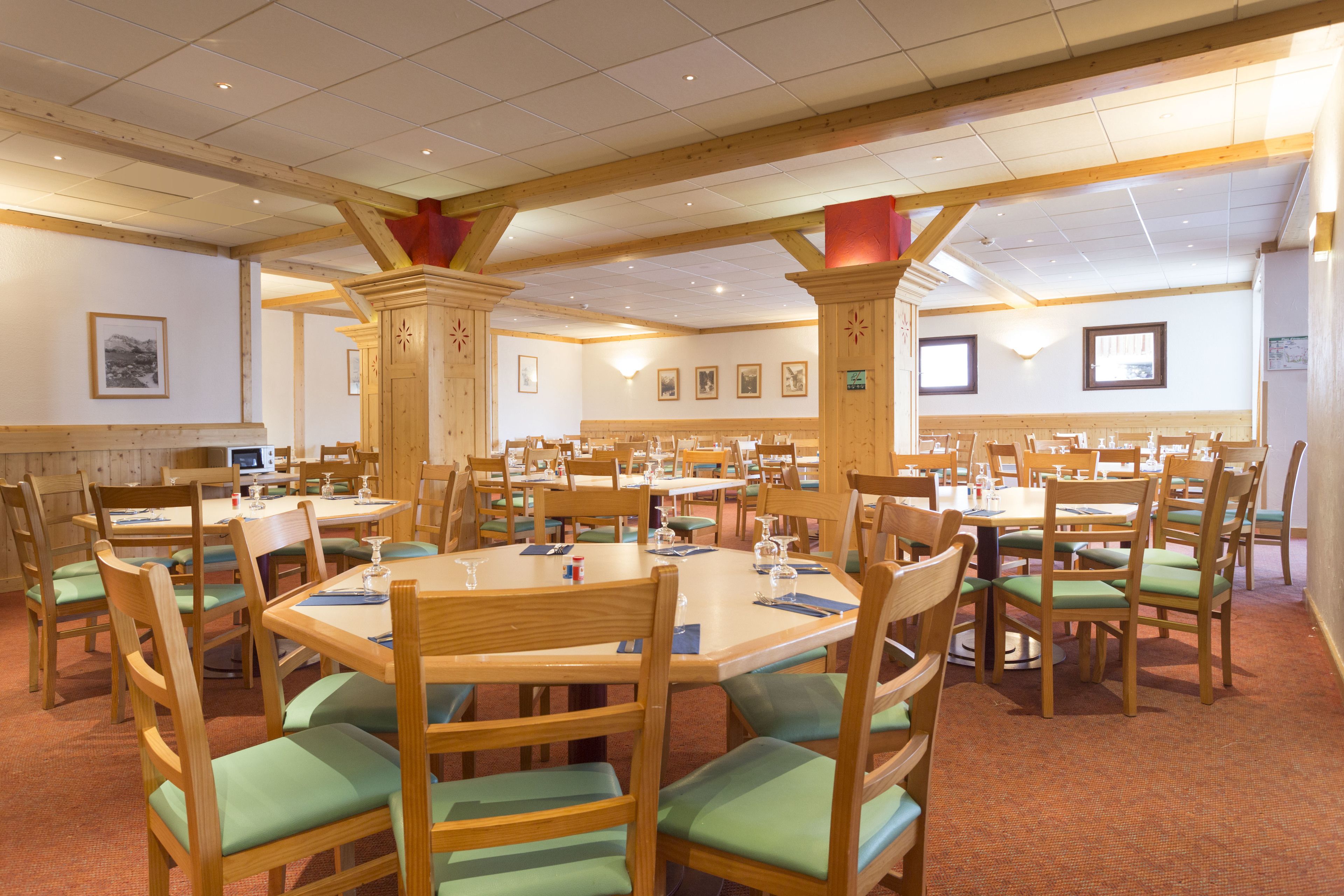 A dining area with multiple tables and chairs, wooden beams on the ceiling, and framed pictures on the walls.