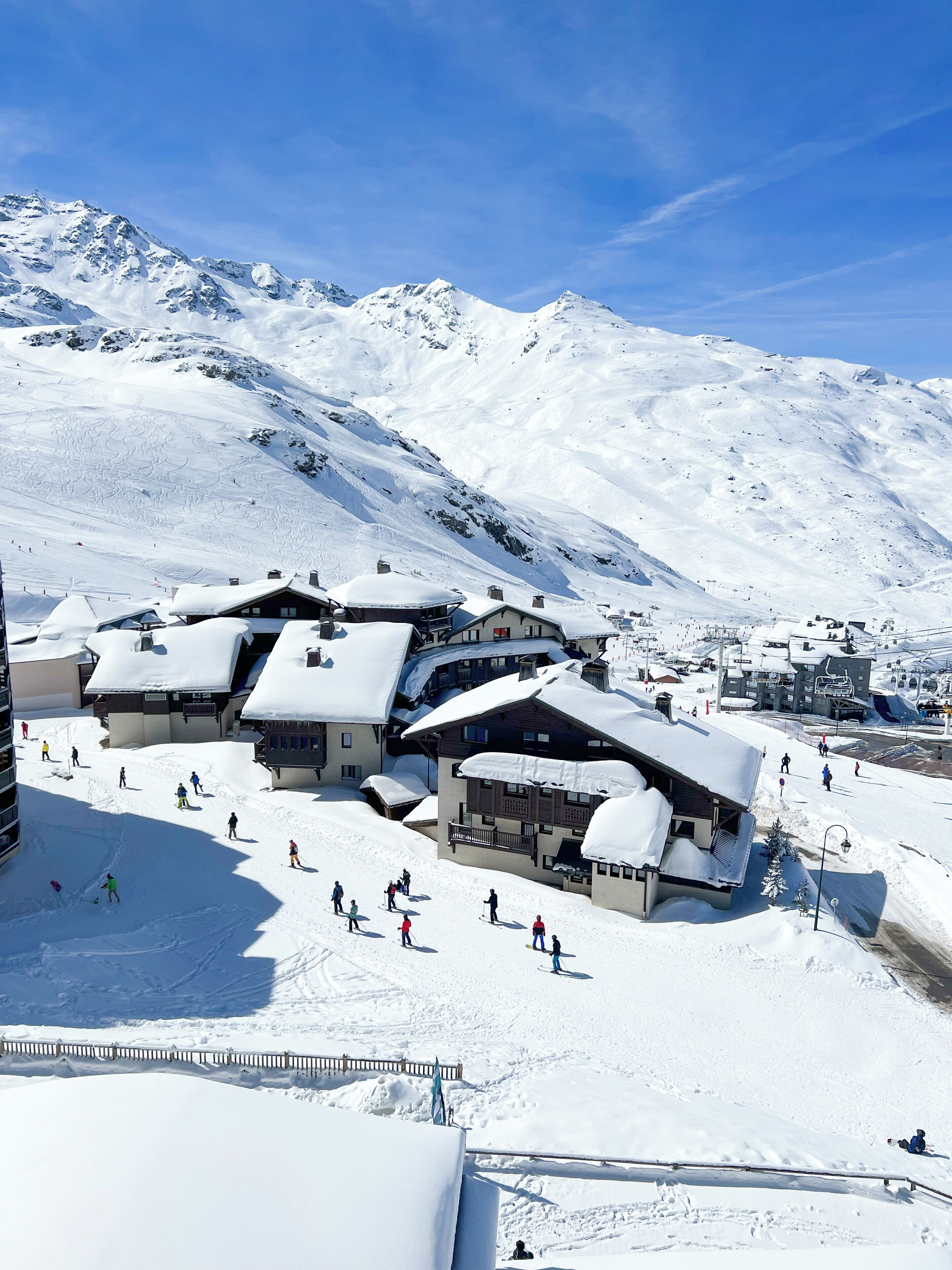 A snow-covered mountain resort with chalet-style buildings, ski slopes, and a clear blue sky.