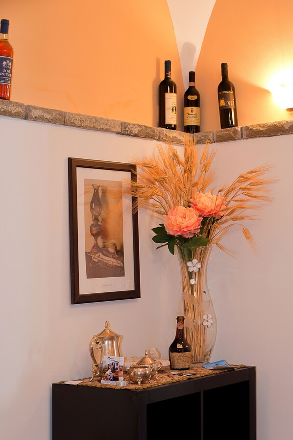 Un meuble à bouteilles, une œuvre d’art encadrée, un vase avec des fleurs et une petite table sur laquelle se trouvent une théière et une bouteille.