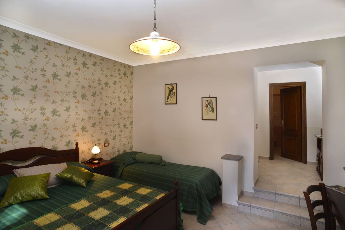 Ein Schlafzimmer mit zwei Einzelbetten, einem Nachttisch mit Lampe, blumigem Wandpapier und gerahmten Bildern an der Wand.
