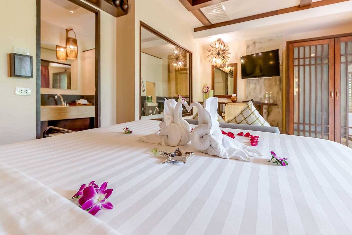 A hotel room with a large bed, a bathroom with a mirror and sink, and a TV mounted on the wall.
