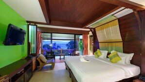 Een hotelkamer met een groot bed, een televisie, een balkon met uitzicht op de oceaan en een houten plafond.