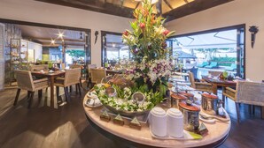 Een hotel lobby met een centraal bloemstuk, een eetgedeelte met rieten stoelen en grote ramen met uitzicht op het omliggende landschap.
