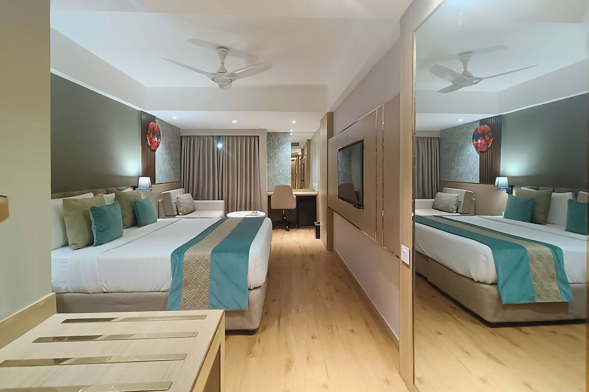 A hotel room with two beds, a desk, a TV, and a ceiling fan.