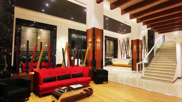 A spacious lobby with a red sofa, black armchairs, a wooden coffee table, and a staircase. - Effotel by Sayaji Indore (Indore)