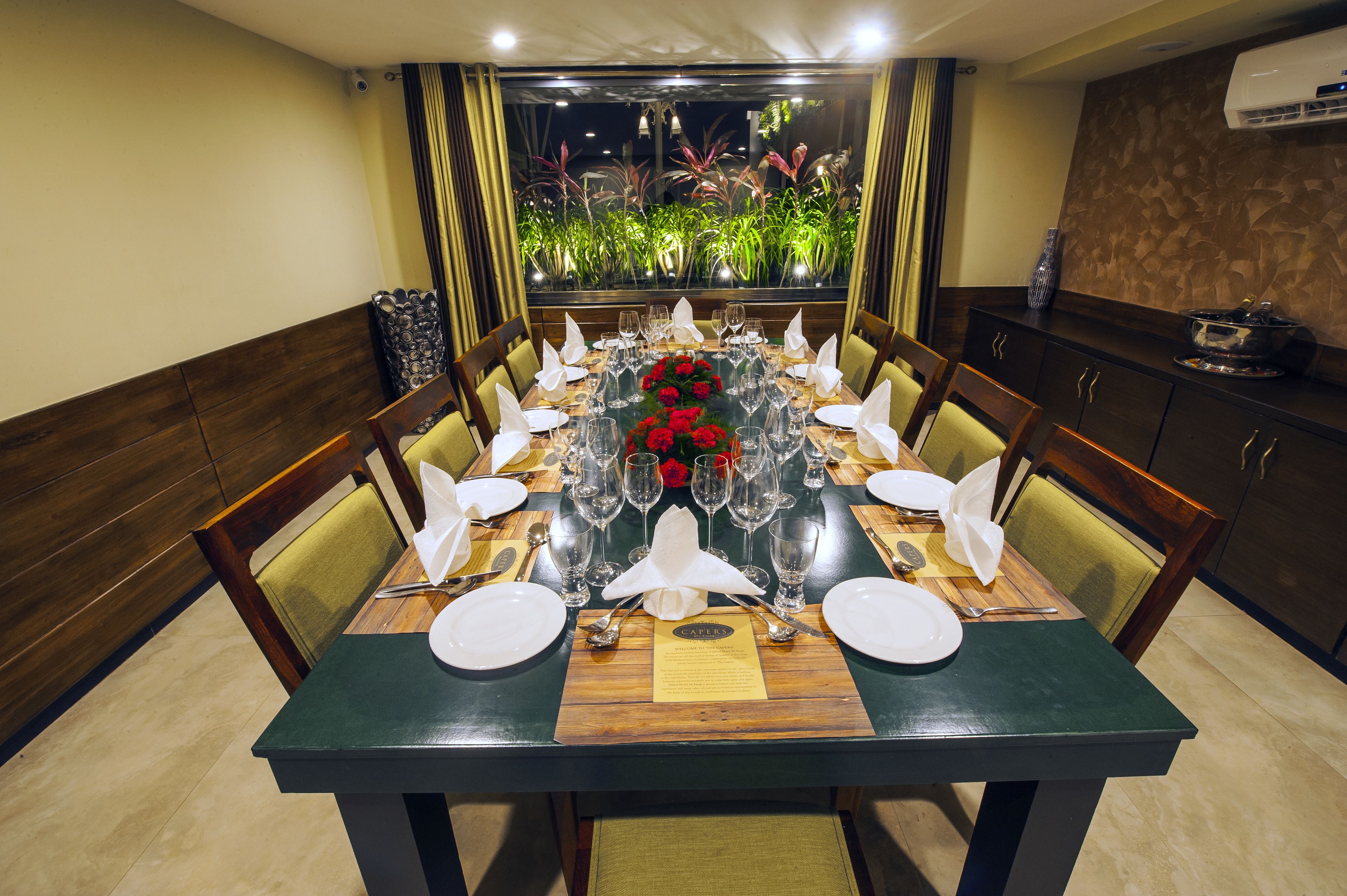 A dining table set for a meal with chairs, a vase of red flowers, and a menu on the table.