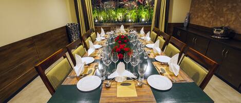 Una mesa lista para una comida, con sillas, un jarrón de flores rojas y un menú sobre la mesa.