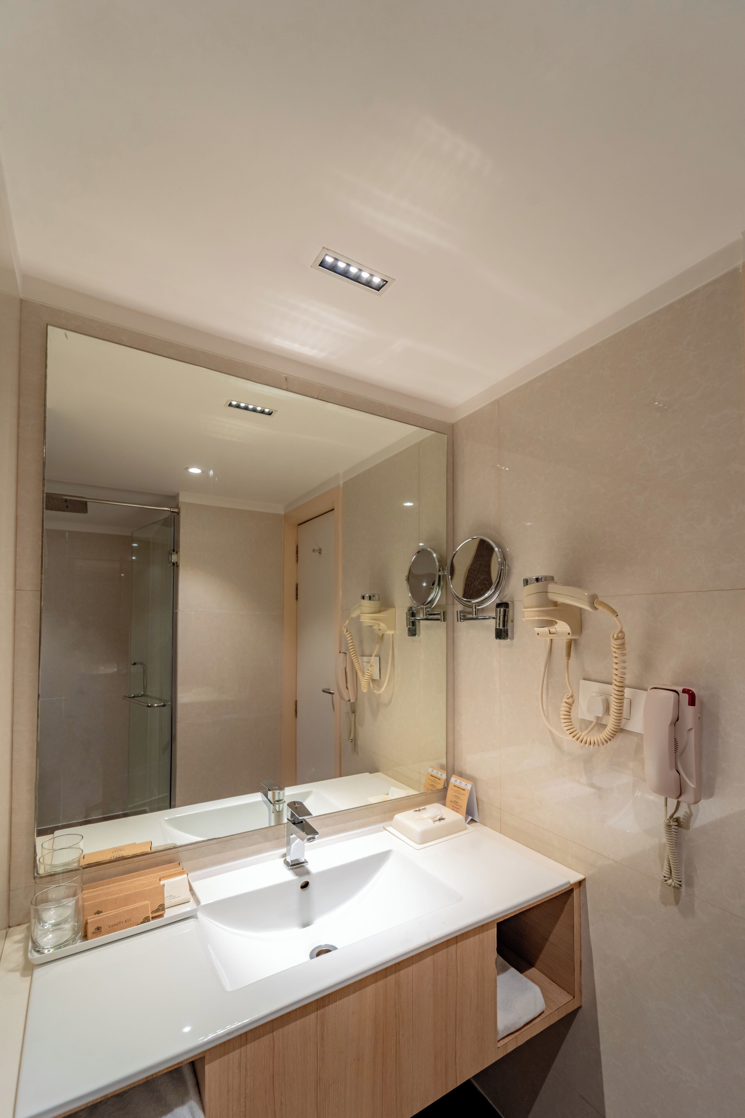 A modern bathroom with a large mirror, a sink, a hairdryer, and a telephone.
