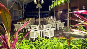 Un área de comedor al aire libre con mesas y sillas de mimbre, rodeada de abundante vegetación.