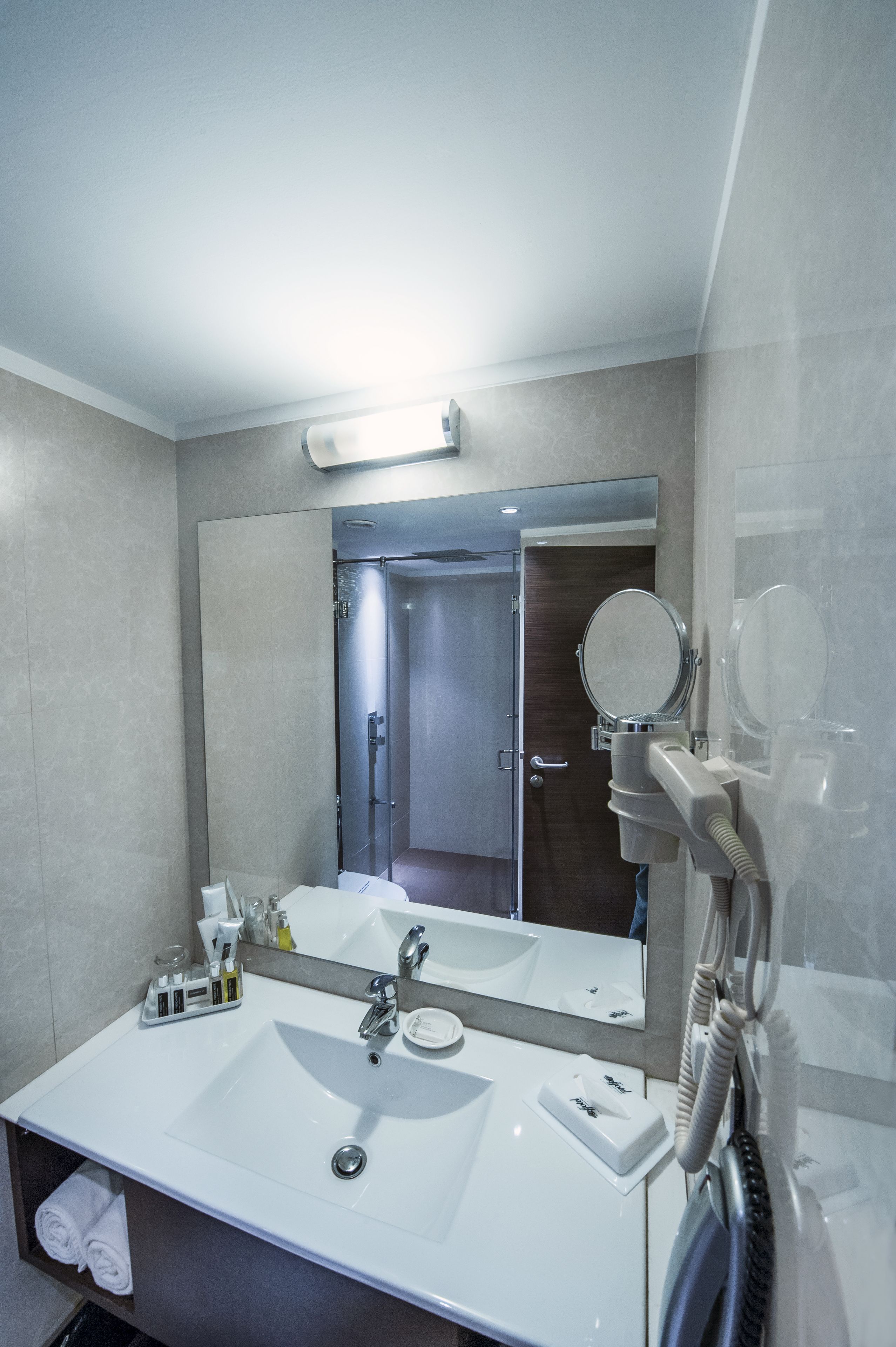 A modern bathroom with a large mirror, white sink, and a hairdryer mounted on the wall.