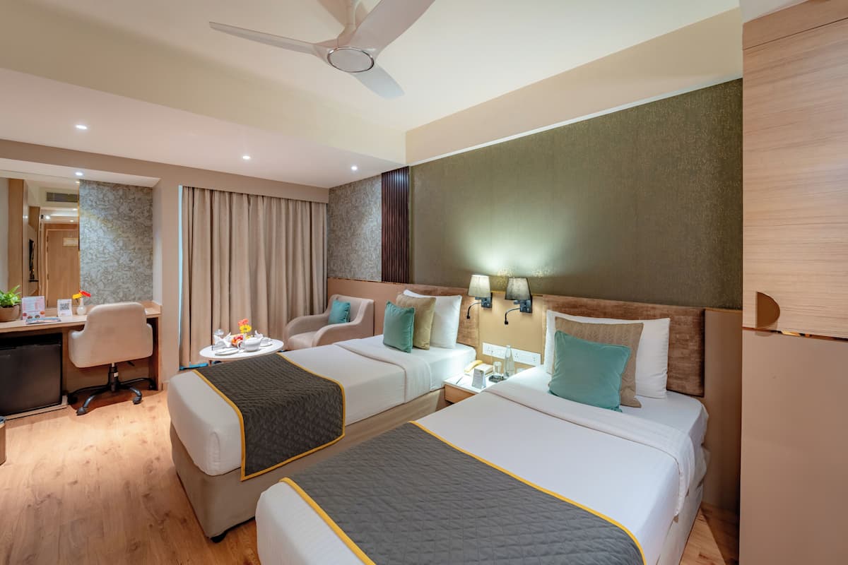 A hotel room with two beds, a desk, a chair, and a ceiling fan.