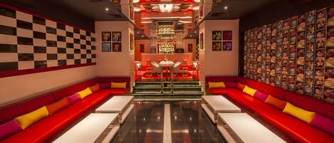 Un bar moderno con asientos rojos, una barra central y una pared de carteles de películas.