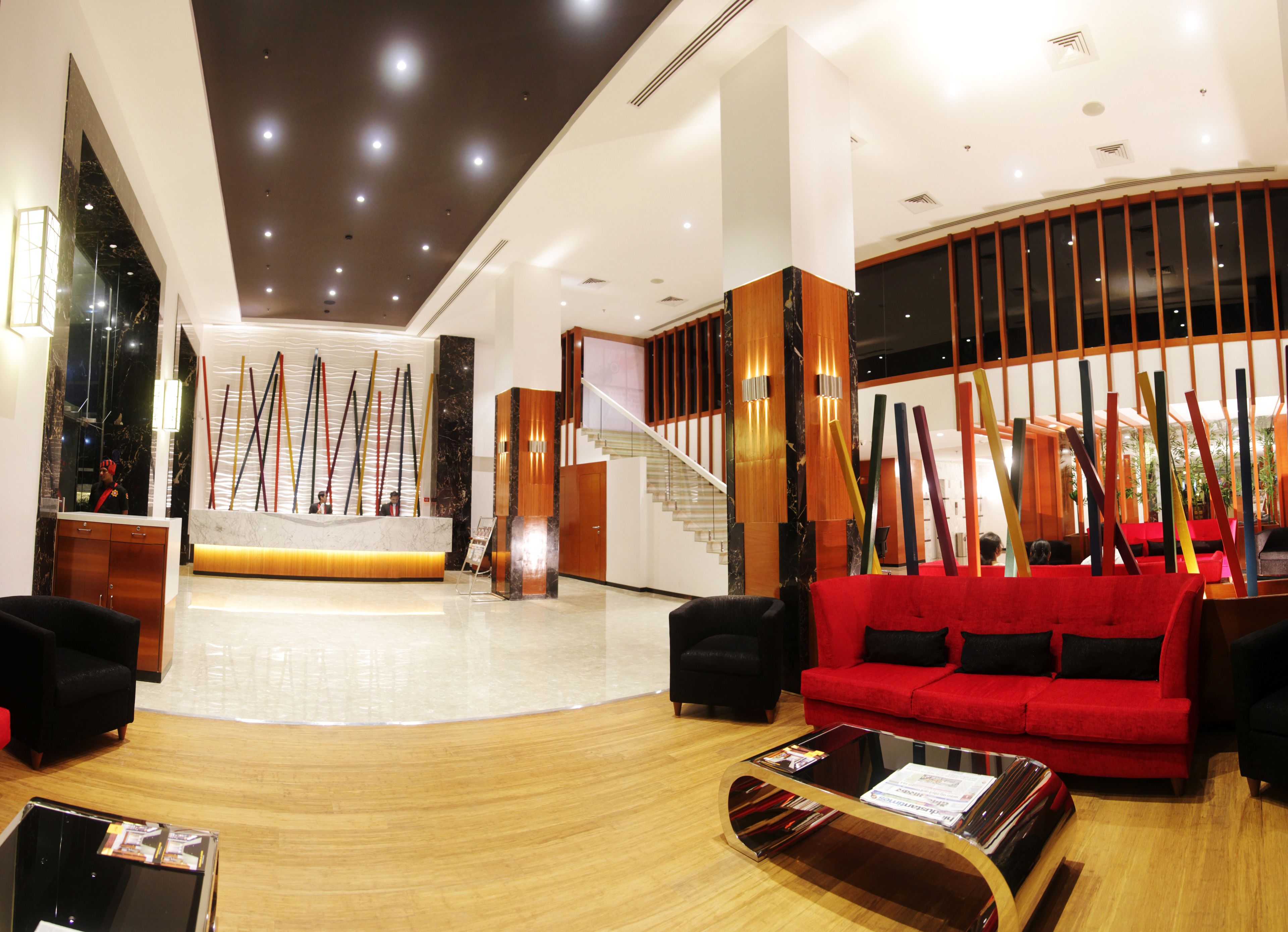 A modern lobby with a reception desk, a staircase, a red sofa, and a glass coffee table.
