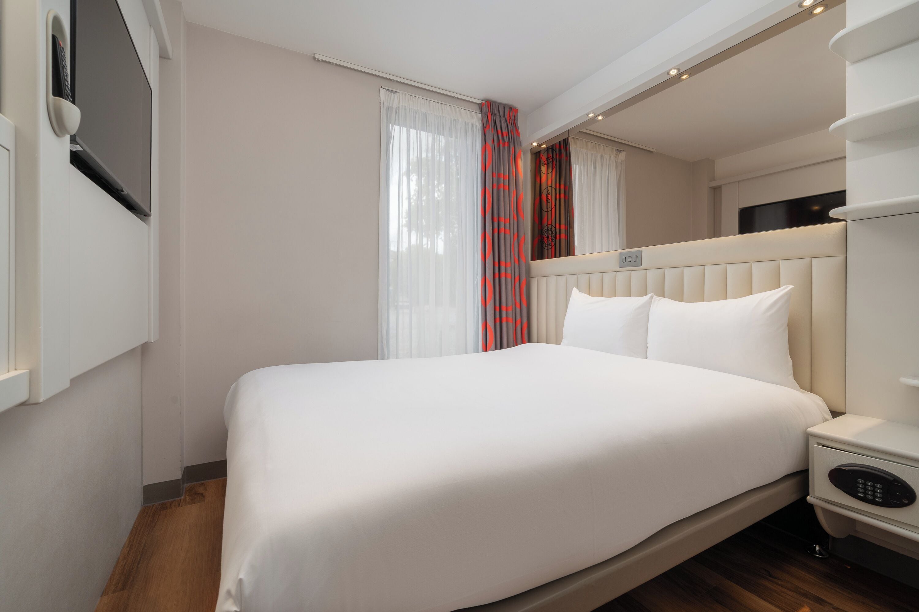 Une chambre d’hôtel avec un lit, une table de chevet, une télévision et une fenêtre avec des rideaux.