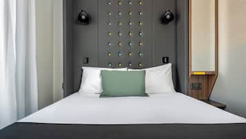 Una habitación de hotel moderna con una cama grande, un cabecero con una cuadrícula de luces, mesitas de noche y una mesita de noche con una lámpara.