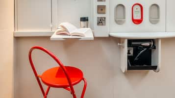Une petite cuisine équipée, avec un plan de travail, une chaise rouge, un livre et un téléphone rouge réservé aux urgences.