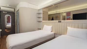 Una habitación de hotel moderna con dos camas, un armario empotrado, un espejo y un televisor montado en la pared.