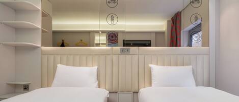 Habitación de hotel con dos camas, un espejo, un televisor y una pequeña estantería.
