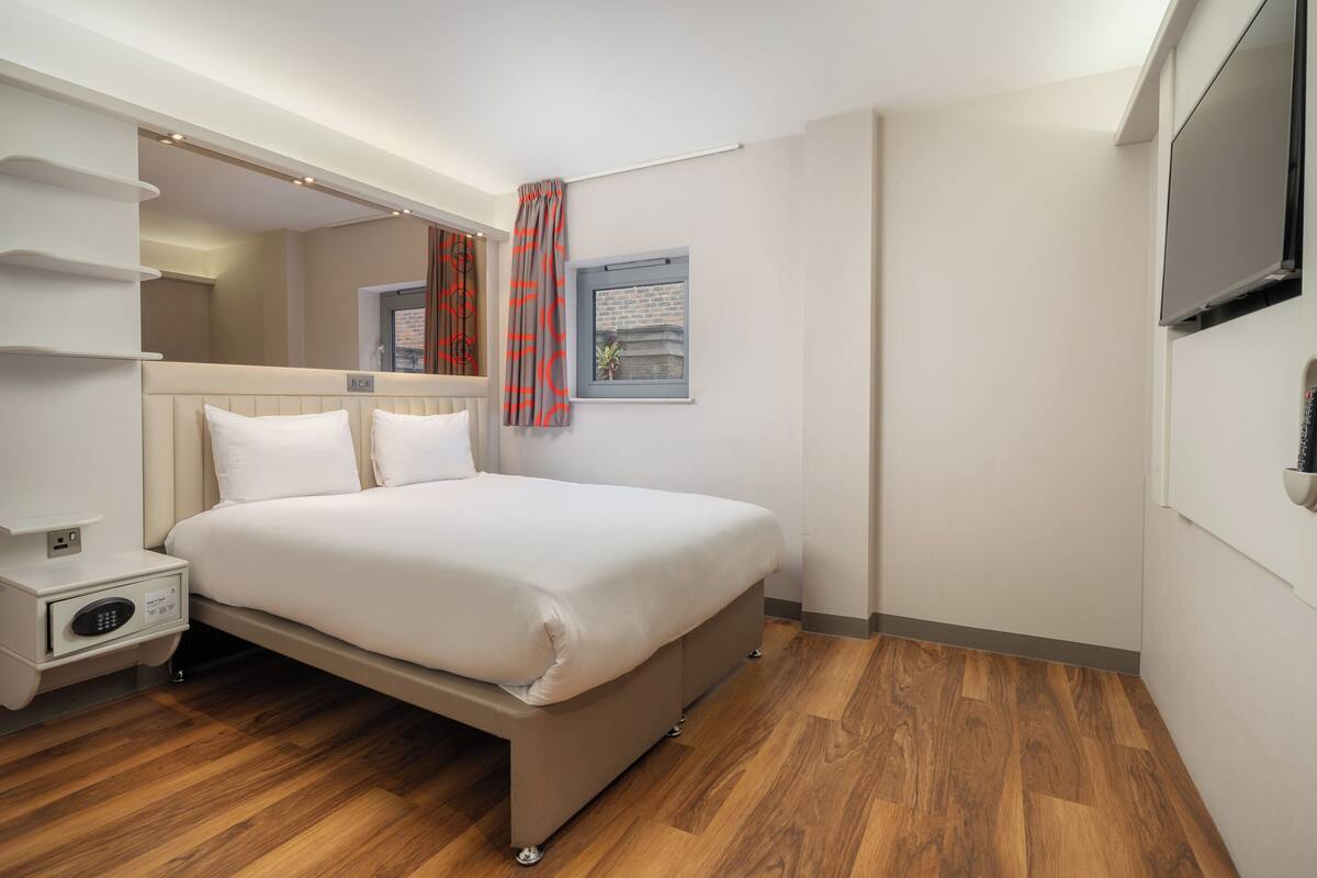 A hotel room with a bed, bedside table, and a television.