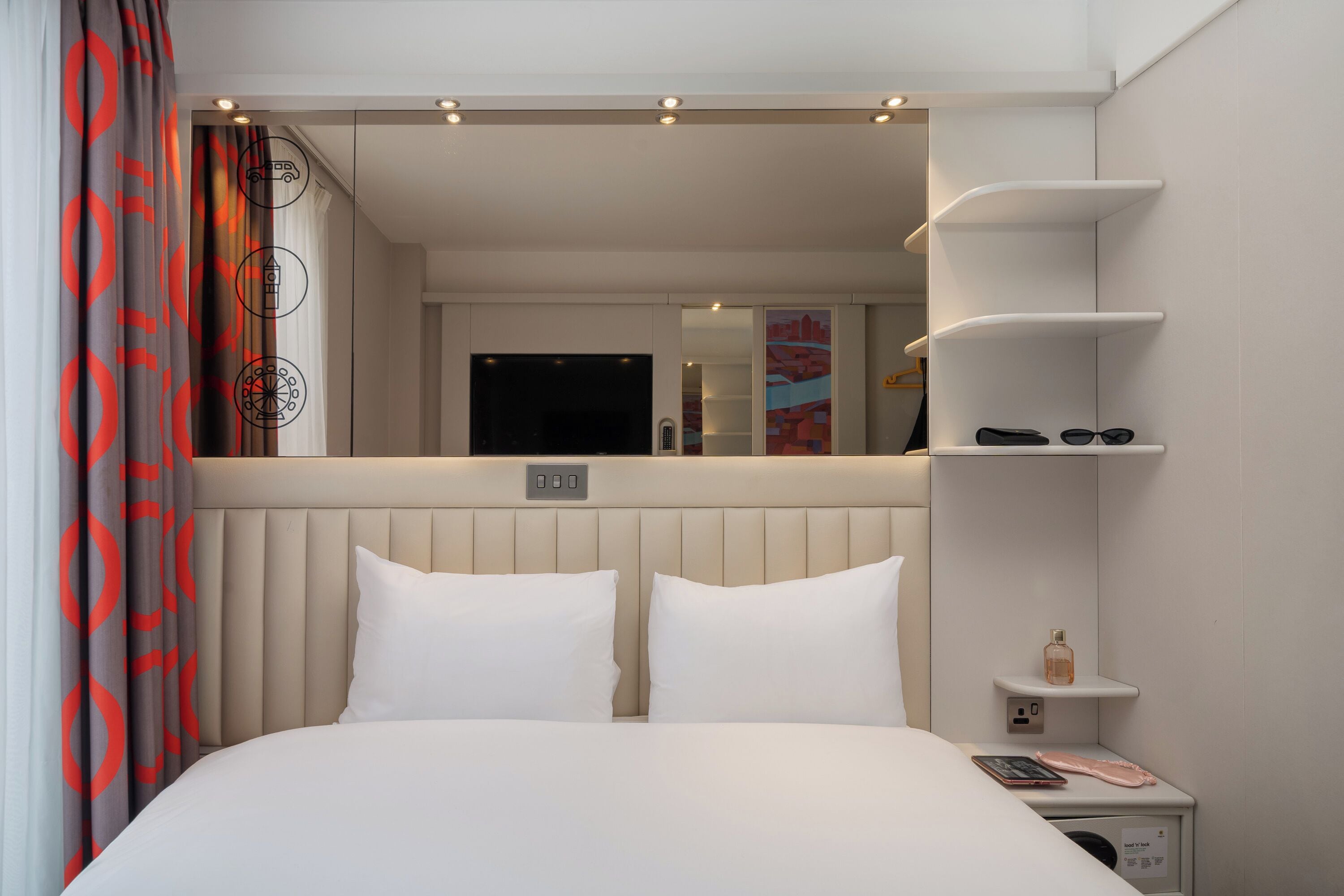 Habitación de hotel con cama, mesita de noche, espejo y vista al pasillo.