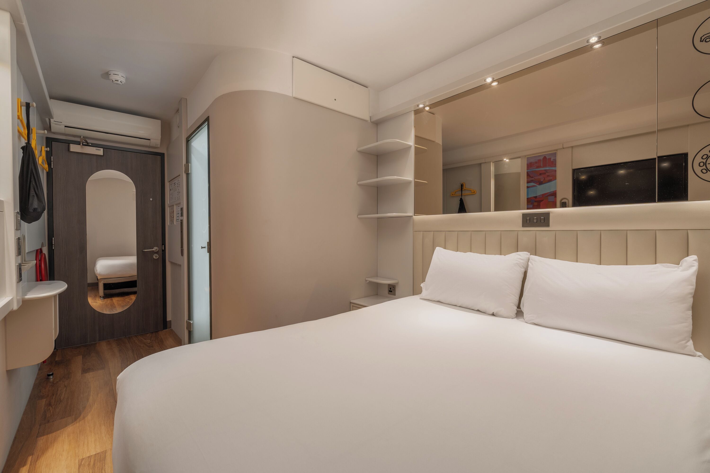 Et moderne hotelværelse med en stor seng, indbygget skab, et spejl og et lille natbord.