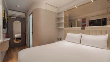 Una habitación de hotel moderna con una cama grande, un armario empotrado, un espejo y una mesita de noche pequeña.