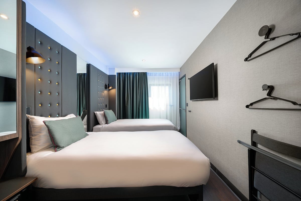 A modern hotel room with two beds, a flat-screen TV, a wardrobe, and a mirror.