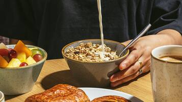 A breakfast setting with a bowl of cereal, a plate of pastries, and a cup of coffee on a wooden table.