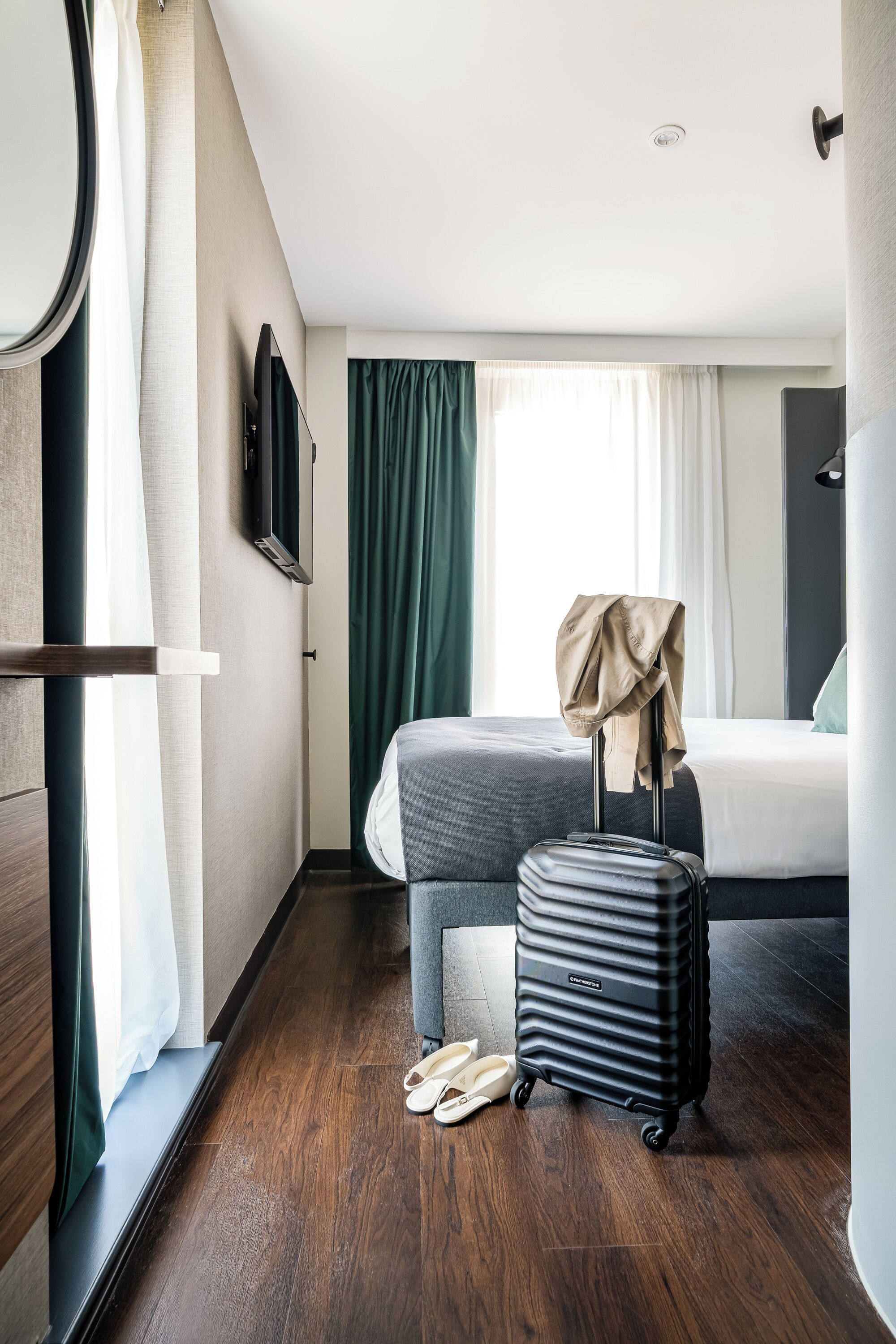 A hotel room with a bed, a suitcase, and a pair of slippers on the floor.