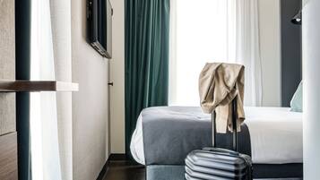 A hotel room with a bed, a suitcase, and a pair of slippers on the floor.