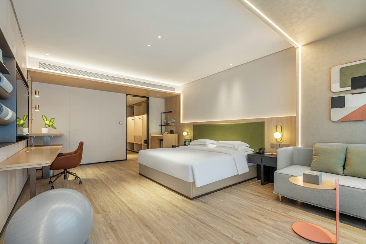 A modern hotel room with a bed, a desk, a chair, a sofa, and a small exercise ball.