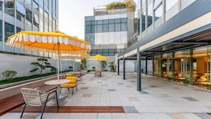 An outdoor seating area with yellow umbrellas, tables, and chairs, surrounded by modern buildings. - EVEN Hotel Hangzhou Yintai City by IHG (Hangzhou)