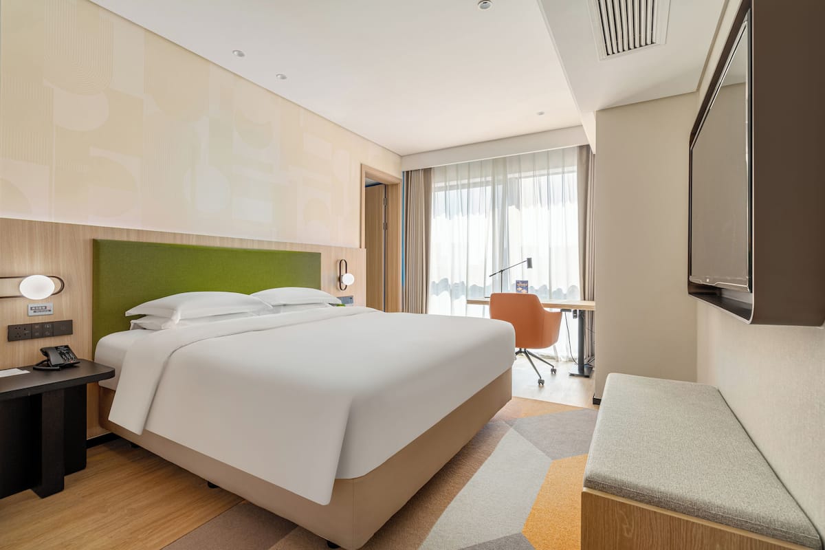 A modern hotel room with a large bed, a desk with a telephone, a chair, and a TV mounted on the wall.