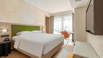 A modern hotel room with a large bed, a desk with a telephone, a chair, and a TV mounted on the wall.