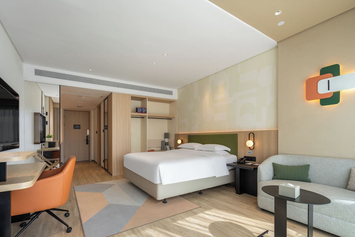 A modern hotel room with a bed, a desk, a chair, a sofa, and a small table.