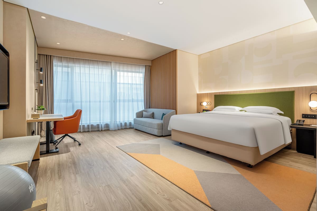 A modern hotel room with a large bed, a desk with a chair, a sofa, and a TV.