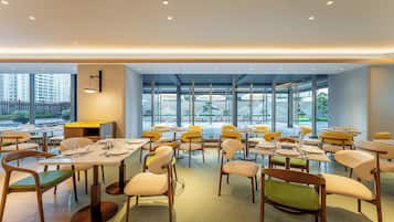 A modern dining area with tables and chairs, large windows, and a view of the city.