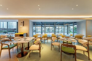 Un comedor moderno con mesas y sillas, ventanas amplias y vistas de la ciudad.