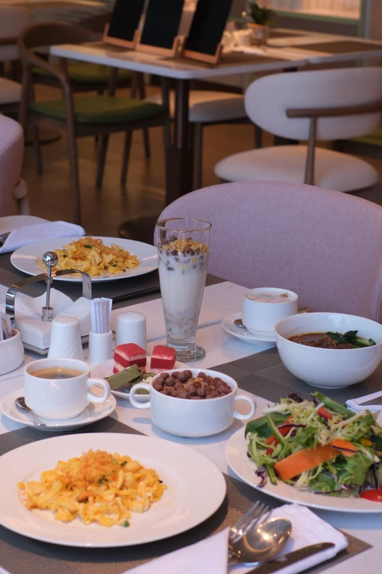 A dining table set with various dishes, including a salad, a bowl of soup, and a glass of milkshake.
