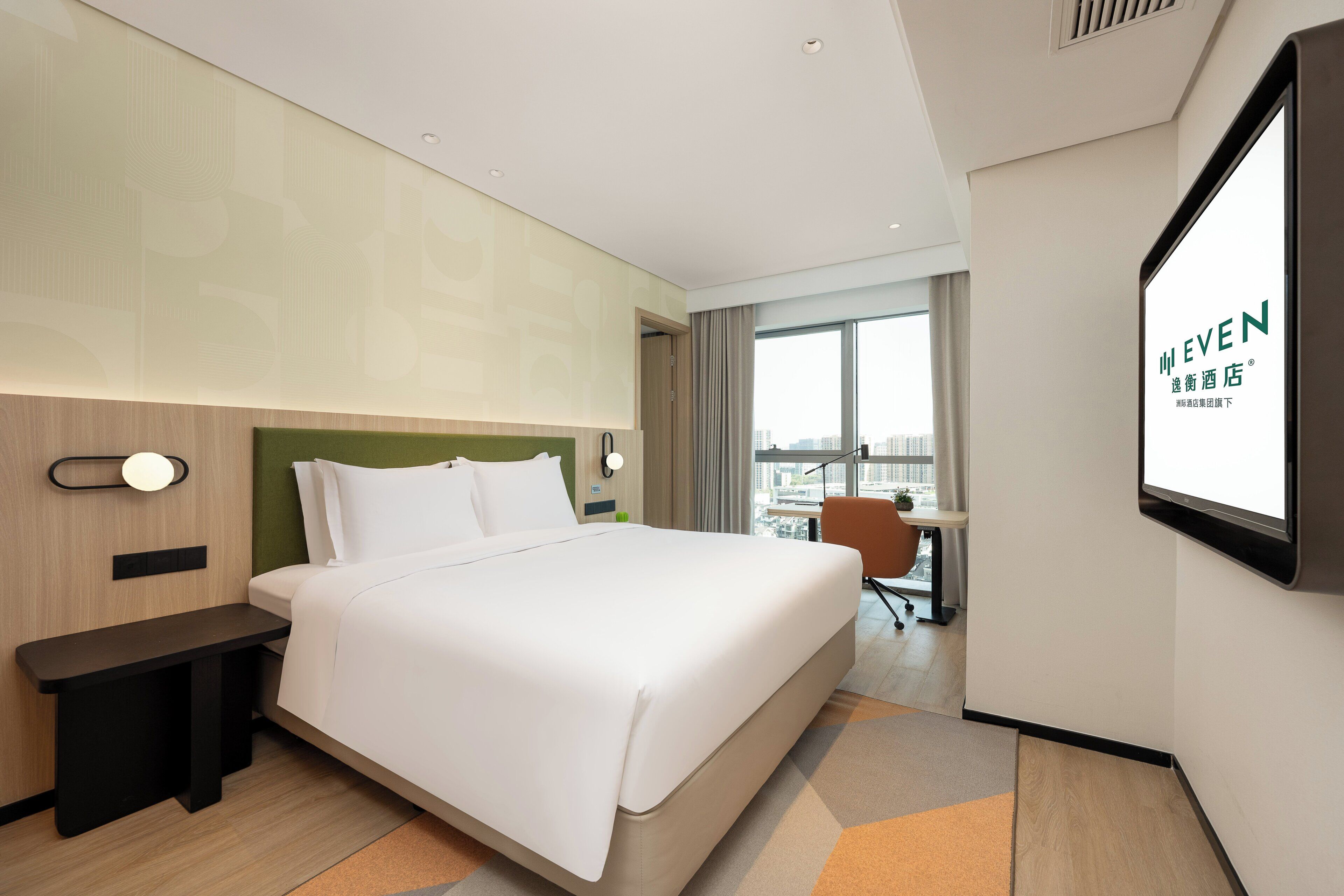 Una habitación de hotel con una cama, una mesita de noche y un escritorio con una silla. Hay una ventana grande que ofrece vistas de la ciudad.