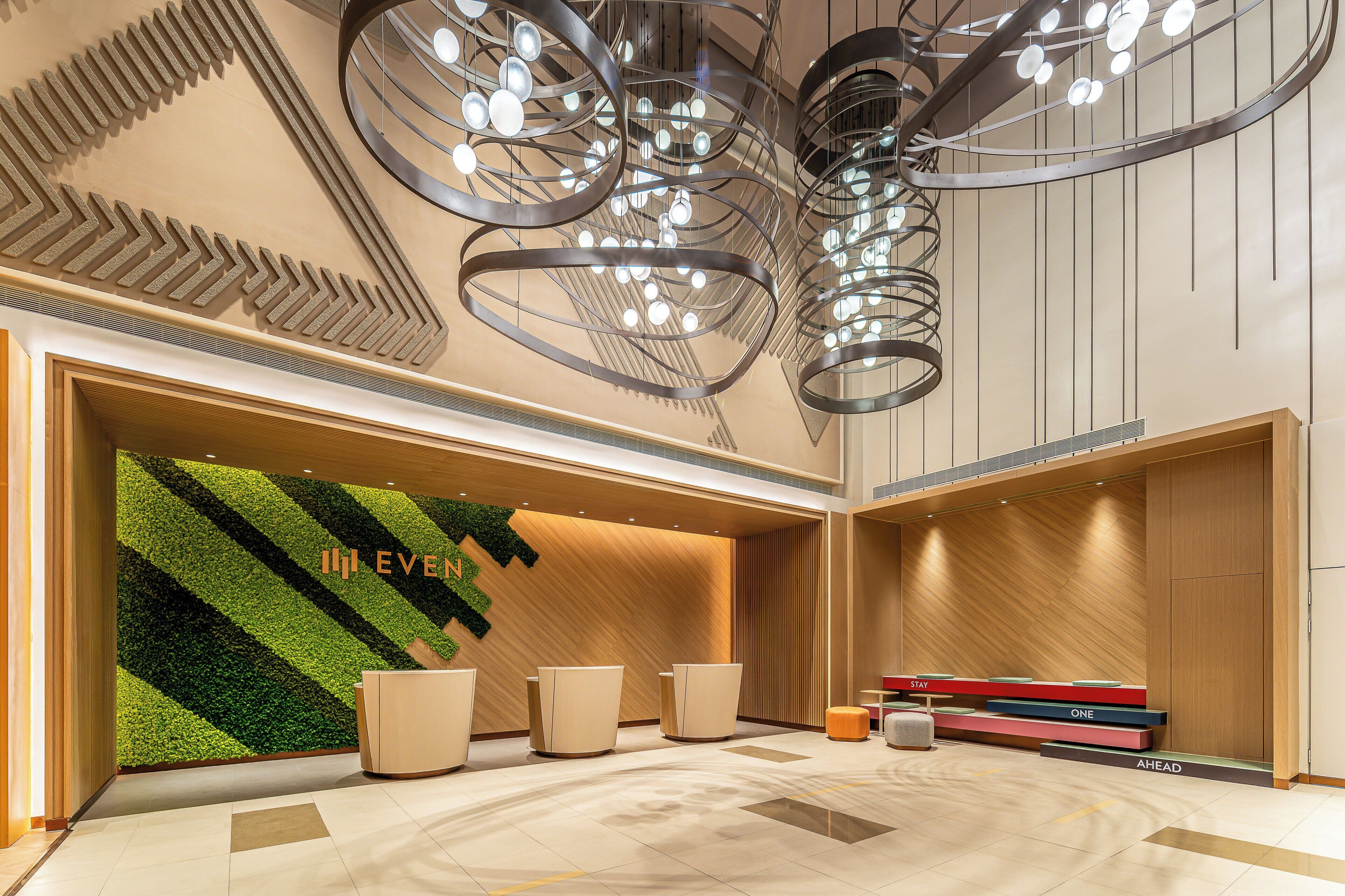 A modern hotel lobby with a green wall, a reception desk, and a seating area.