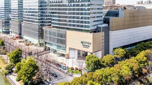 Un edificio moderno con fachada de vidrio, un cartel que dice 'WEVEN', y un parque circundante con árboles.