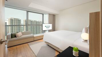 Een hotelkamer met een groot bed, een bank, een televisie en uitzicht op hoogbouw.