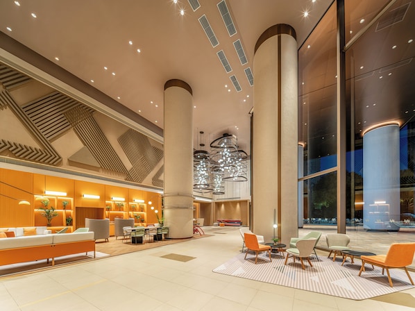A spacious lobby with high ceilings, a central column, and a modern chandelier.