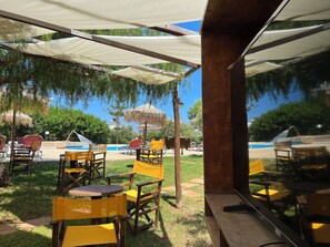 An outdoor seating area with tables and chairs, a pool, and umbrellas. - Portokali Apartments (Hersonissos)