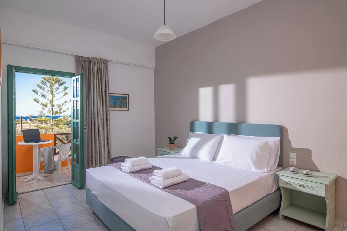 Une chambre d’hôtel avec un lit, une table de chevet avec une lampe, une fenêtre avec des rideaux et une vue sur l’extérieur.