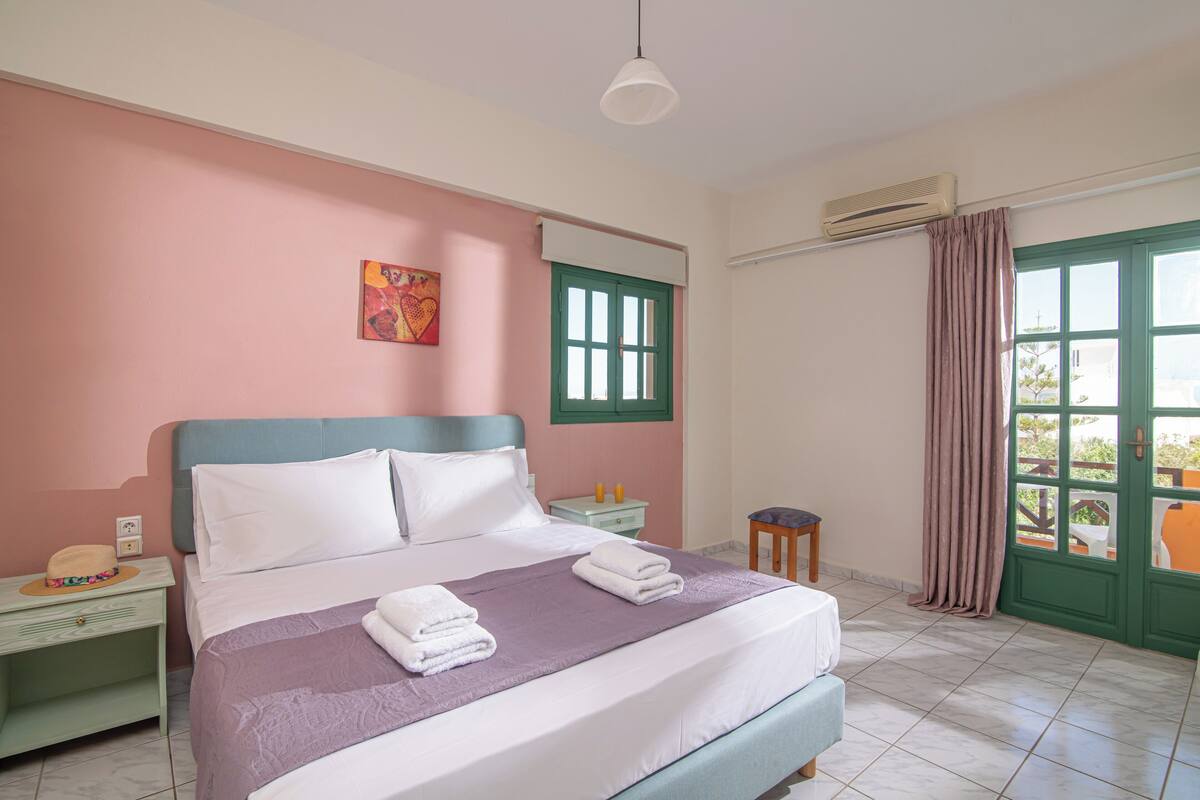 Une chambre à coucher avec un lit, une table de chevet, une fenêtre avec des rideaux et une vue sur l’extérieur.