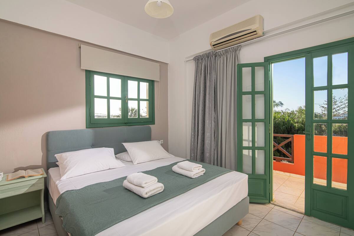 Une chambre à coucher comprenant un lit, une table de chevet, une fenêtre avec des rideaux et un appareil de climatisation.
